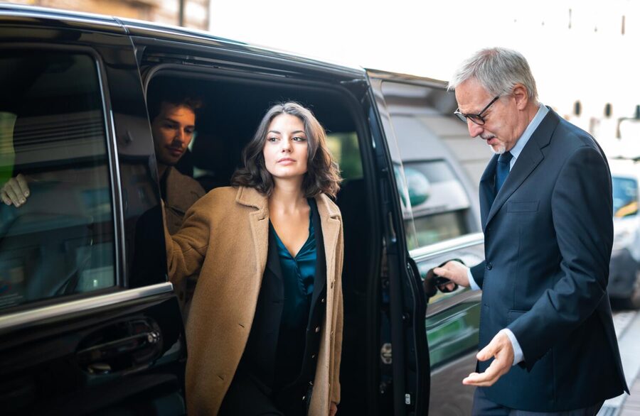 Conductor recibiendo a dos pasajeros junto a una van negra